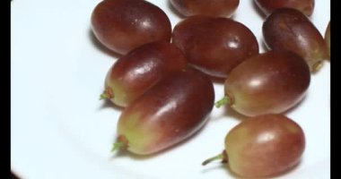 Tabakta üzüm var. Beyaz bir tabakta bir demet mor üzüm. Beyaz tabak dönüyor.