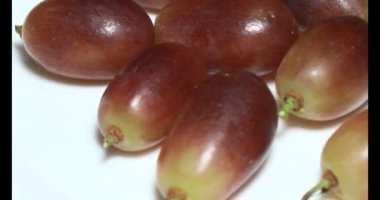 Tabakta üzüm var. Beyaz bir tabakta bir demet mor üzüm. Beyaz tabak dönüyor.