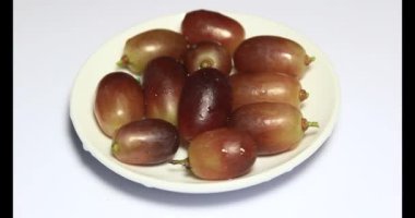 Tabakta üzüm var. Beyaz bir tabakta bir demet mor üzüm. Beyaz tabak dönüyor.