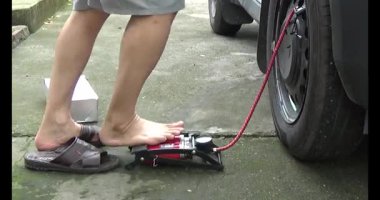 Adam araba lastiği pompalıyor.