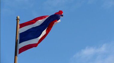 Tayland bayrağının kırmızı, beyaz ve mavi çizgileri açık mavi gökyüzü arka planında rüzgarda dalgalanıyor.