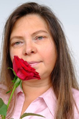 Uzun saçlı, elinde kırmızı güller olan mutlu, olgun bir kadın. Düşünceli, düşünceli, konsept bir anne. Sevgililer günü, doğum günü, yüzün üst kısmı yakın plan, seçici bir odak noktası.