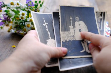 Kadın elleri 1950 'lerin klasik fotoğraflarını parmaklıyor, masadaki fotoğraflar, yabani çiçekler, soy ağacı konsepti, atalarımızın hafızası, aile ağacı, nostalji, çocukluk anıları, hatırlama.