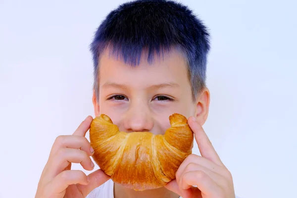 孩子们的近照 蓝头发的男孩紧握着玫瑰烤羊角面包 手拉着嘴 表现出欢快的笑容 概念美味的早餐 快乐的童年 情感发育的孩子 — 图库照片