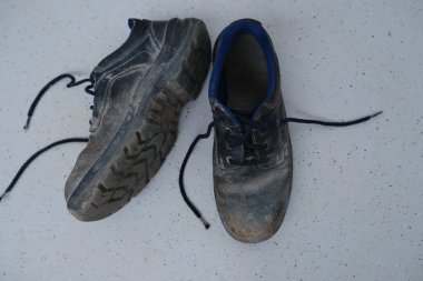 Yakın plan çizikler, kirli siyah güvenlik ayakkabıları, açık gri zeminde bağcıkları olan eski püskü iş deri botları, özel koruma giysisi konsepti, profesyonel ayakkabılar, iş güvenliği
