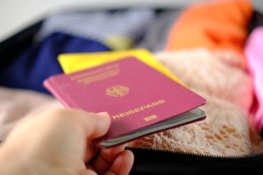 Kadın pasaportunun yakın plan çekimi, CVID sertifikası, açık bavulda katlanmış giysiler, eşyalar, belgeler, tatil için gardırop toplama konsepti, iş seyahati, uzun zamandır beklenen yolculuk.