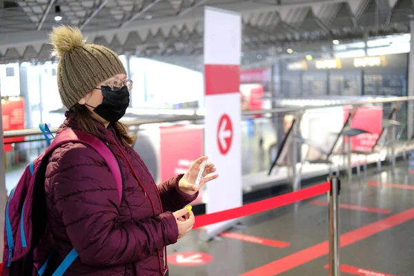 middle-aged woman years old in burgundy jacket and medical mask holds test tube for covid-19 antigen test in airport building, mandatory test for boarding airplane flight during coronavirus pandemic