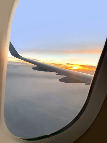 view from window on airplane wing plane while flying above dawn clouds, sun rises on horizon, plane flies over sea, ocean, transportation passengers, heavenly space, meditative calmness