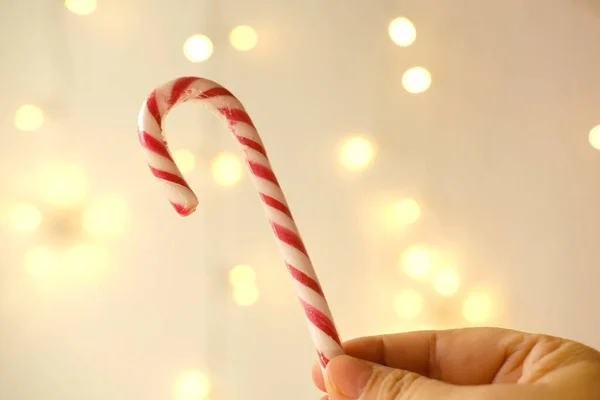 close-up female hand holds candy cane, traditionally white with red stripes cane-shaped stick candy, Christmastide, Saint Nicholas Day concept, new year celebration, happy childhood, sweet life