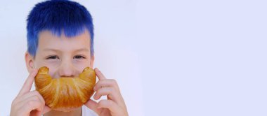close-up of child's face, boy of 8 years old holds rosy baked croissant with hands near mouth, depicts cheerful smile, concept delicious breakfast, happy childhood, emotional development children