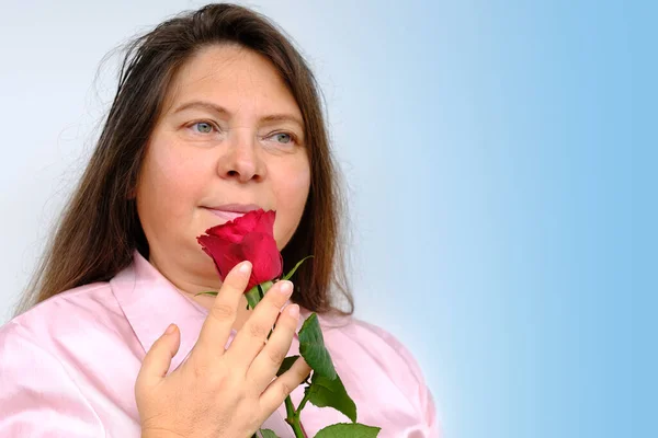 happy romantic mature woman with long hair holding bouquet of red roses in her hands, looking thoughtfully, concept mother\'s, Valentine\'s day, birthday, upper part of face close-up, selective focus