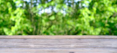 wooden table in garden, beautiful blurred natural landscape in background with green foliage and soft sunset transparenting through branches, long panorama, concept cozy mood, blank for designer