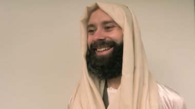 Jesus Christ, young pensive bearded man smiling, cheerful guy 30 years in light vestment, beige cape stands in image of Savior, concept Holy Scriptures of Old and New Testaments, forgiveness of sins