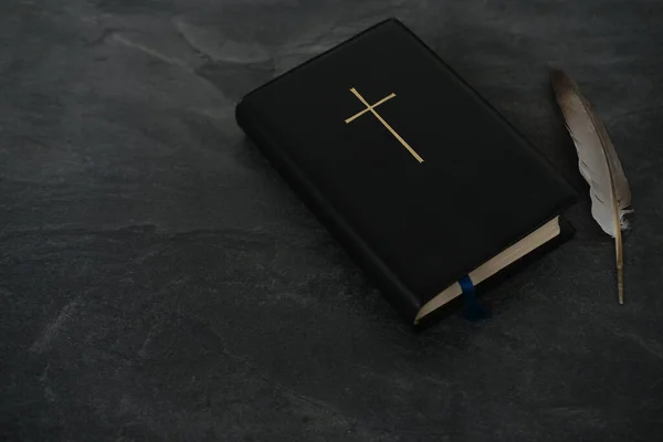 old black book, family bible in dark cover, golden cross, goose feather, concept of intermediary between God and world, eternal Christian values, all saints\' day, unity of people in faith