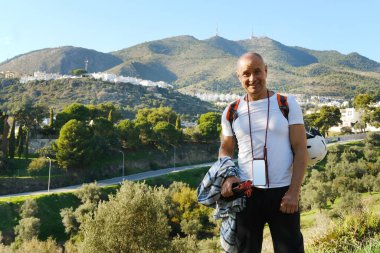 elderly, charismatic mature satisfied man 60 years old, tourist with backpack on back and mobile phone on cord walks along road with magnificent natural scenery, watching nature, travel, vacation