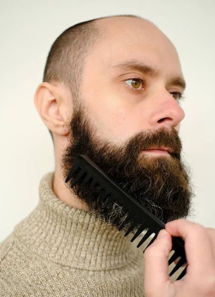 close-up of male face, young bearded and mustachioed man, guy with 25 - 30 years combs his thick beard, concept of mustache and beard stubble care products, hairline hygiene on lower part of face