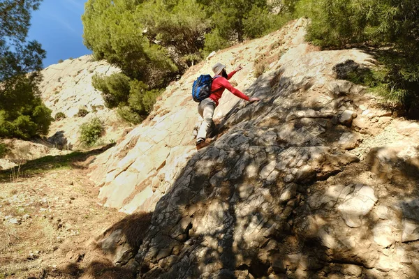 若い観光客 バックパック付きオレンジジャケットの男は崖を登る ロッククライマー 極端な人々のライフスタイル 到達目標の概念 生命保険 ハイキングの難しさ 極端なスポーツ — ストック写真