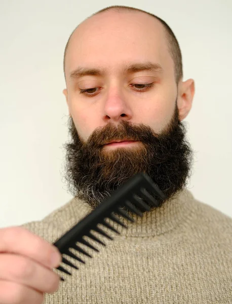 close-up of male face, young bearded and mustachioed man, guy with 25 - 30 years combs his thick beard, concept of mustache and beard stubble care products, hairline hygiene on lower part of face
