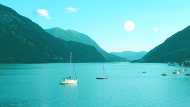 Avusturya 'daki Achensee gölünde yüzen güzel tekne ve yatlar, durgun suların üzerinde yükselen yeşil dağlar, akşam manzarası, rezervuarlı tatil konsepti, tatil yeri Tyrol