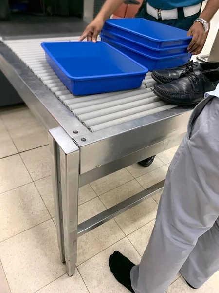 passenger put his shoes on conveyor, airport security personnel takes plastic containers for gadgets, bags, boxes on way to X-ray machine airport checkpoint, air travel security requirement