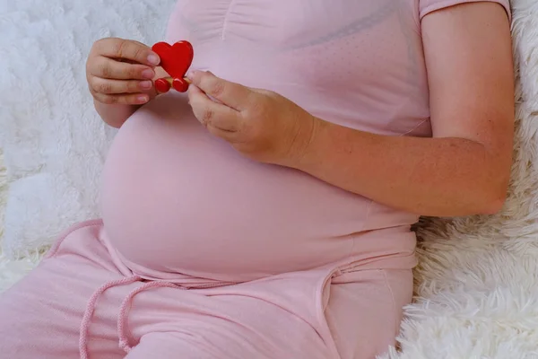 中年妊娠中の女性ピンクのTシャツは 彼女の腹の近くに赤い心を保持しています 新生児を待っています 妊娠再生の概念 体外受精で 幸せな母親 選択的フォーカス — ストック写真