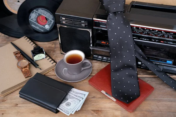 old radio receiver with a tape recorder, vinyl music discs, black tie, e-book in a leather case, money in a purse, wrist watch, a cup of tea, coffee, men\'s style concept, father\'s day