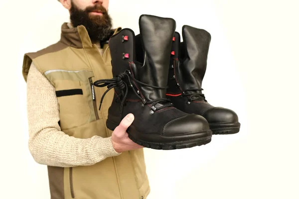 pair black Safety Shoes, work boots made of leather with reinforced cape, high top in hands of young bearded man, builder in uniform, concept of highest product quality, professional workwear