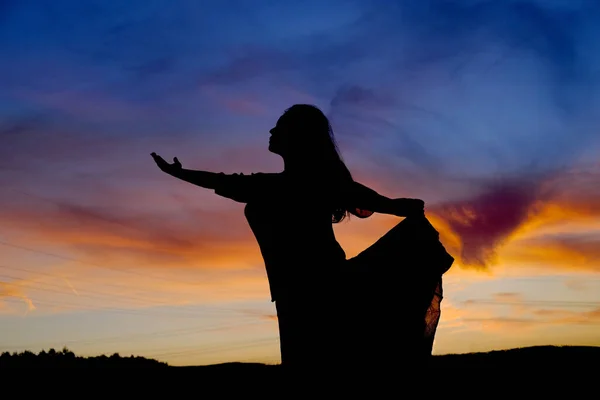 stock image black silhouette of woman with long hair in delight raises her hands at sunset in a field with silhouette of hills, mountains and colored sky in background, concept of happiness, unlimited freedom