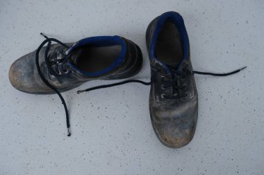 Yakın plan çizikler, kirli siyah güvenlik ayakkabıları, açık gri zeminde bağcıkları olan eski püskü iş deri botları, özel koruma giysisi konsepti, profesyonel ayakkabılar, iş güvenliği