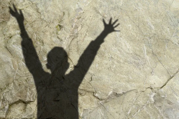 blurred black shadow of child with raised hands in a pleading gesture against background of on gray natural stone wall, the concept of domestic violence, a victim of abuse