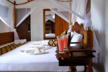 cozy bedroom with mosquito net, white mesh canopy, two glasses of fresh juice by wooden bed in apartment room, hotel, enjoys vacation in tropical country, quench your thirst on hot day
