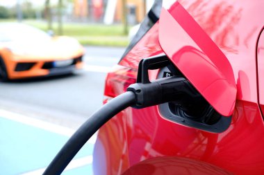 Sokakta kırmızı renkli araba, kablo ile elektrik yükleme, Avrupa şehrinde elektrikli araç, enerji silindirik akülatörler, alternatif enerji gelişimi, teknoloji ve yenilik