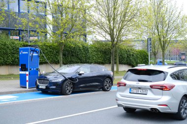 Elektrikli araç kabloyla şarj oluyor, Avrupa 'da anaova şarj istasyonu, caddede araba melezi, alternatif enerji, teknoloji, yenilik, FRANKFURT - Nisan 2023