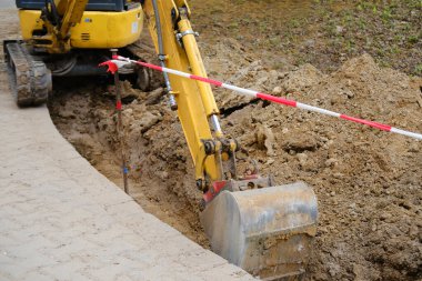 Kazı kovası toprağı sokak siperlerinde kazıyor, kentsel iletişimi onarma konsepti, binalara elektrik şebekeleri kurma, yer altında iletişim için optik fiber döşeme