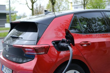 Kırmızı Volkswagen araba hibrid caddede, elektrik kablolu ile şarj Avrupa şehrinde elektrikli araç, alternatif enerji geliştirme, teknoloji ve yenilik, FRANKFURT - Nisan 2023