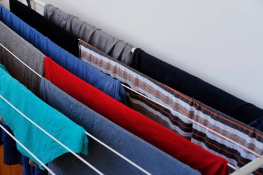 close-up of wet laundry hanging and drying on a wire room dryer, home chores concept, cleaning clothes, proper washing of cotton colored fabrics, selective focus at shallow depth of field