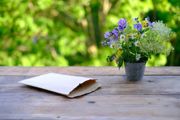 古い紙の封筒 庭のテーブルの上の野生の花の花束 緑の葉と美しいぼやけた自然の背景 系譜の概念 記憶の祖先 家族のアーカイブ — ストック写真
