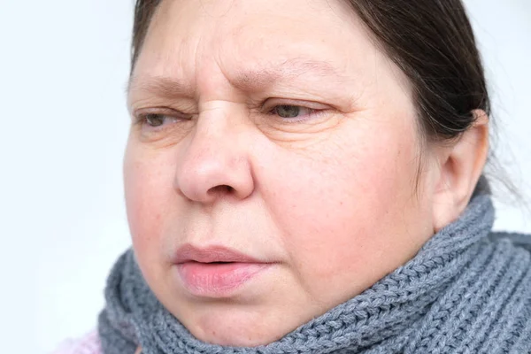 stock image close-up face of mature woman 55 years face, neck wrapped in scarf, sick person with inflamed eyes suffering from pain, malaise due to illness, concept of fever, bad mood, discontent, sore throat