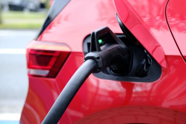 Sokakta kırmızı renkli araba, kablo ile elektrik yükleme, Avrupa şehrinde elektrikli araç, enerji silindirik akülatörler, alternatif enerji gelişimi, teknoloji ve yenilik