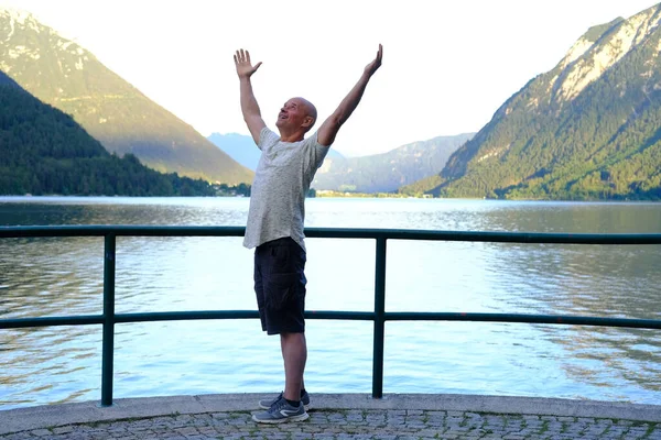 Yaşlı, olgun bir adam sabah doğasını, dağ manzarasını, Avusturya 'daki Achensee kıyı gölündeki yogayı, sakin, geniş suların üzerindeki yeşil dağları, rezervuarın yanındaki tatili, tatil yeri Tyrol' u sever.