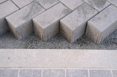 gray paving blocks on the ballast, side view, construction site of pavement modern granite cobblestone road in city center, roadworks stonework at pedestrian area, concept installation, renovation