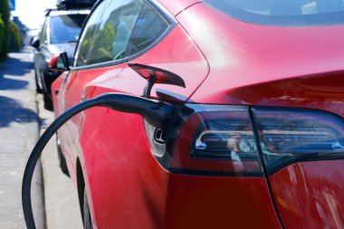 Sokakta kırmızı renkli araba, kablo ile elektrik yükleme, Avrupa şehrinde elektrikli araç, enerji silindirik akülatörler, alternatif enerji gelişimi, teknoloji ve yenilik
