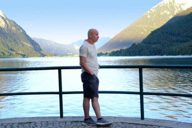 Yaşlı, olgun bir adam sabah doğasını seviyor, düşünüyor, dağ manzarasını, Avusturya 'daki Achensee Gölü' nü, geniş suların üzerinde yeşil dağlar yükseliyor, rezervuar ile tatil, aktif seyahat, tatil yeri tyrol