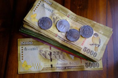 Sri Lanka ulusal para birimi, kağıt para faturaları 5000 Rupi banknotlar, ahşap masa üzerinde sikkeler, devalüasyon, yüksek enflasyon, seyahat, tatil, tasarruf, bankacılık, vergi ödeme kuru