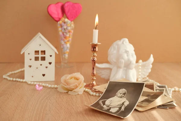 stack of vintage photos on table, romantic still life in love style, in vase red hearts on sticks, cupid with wings, model house, candles burning, concept of family tree, genealogy, childhood memories