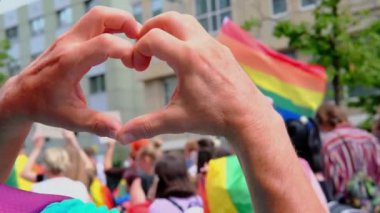 Uluslararası LGBT hareketinin katılımcılarına karşı erkek eli kalp şeklinde yakın çekim, gökkuşağı bayraklı Gay Onur Yürüyüşü, Gurur Ayı, lezbiyen ve gay insanların toplu yürüyüşü