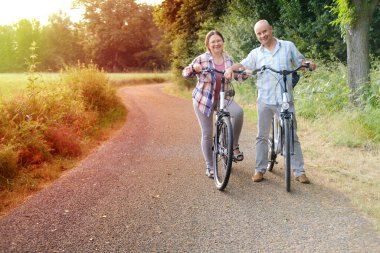 Yaşlı, olgun bisikletli kadın ve erkek, parkta mutlu bir çift, ortak bisiklet sürüşleri, doğal güzellikler bisiklet turu, hayat dolu anlar.