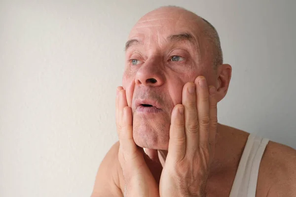 特写有魅力的成熟男子60岁时在脸上涂上剃须后护理 批判性地检查面部 因年龄变化而烦躁不安 中年危机 选择性焦虑症 — 图库照片