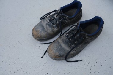 Yakın plan çizikler, kirli siyah güvenlik ayakkabıları, açık gri zeminde bağcıkları olan eski püskü iş deri botları, özel koruma giysisi konsepti, profesyonel ayakkabılar, iş güvenliği