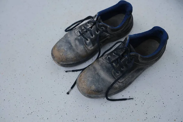 stock image close-up of pair old scratched, dirty black Safety Shoes, shabby work leather boots with laces on light gray floor, concept of special protective workwear, professional shoes, work safety